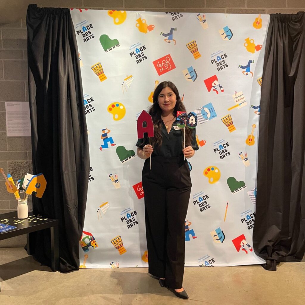 Young business professional standing in front of a 50th anniversary photo backdrop holding up props. She is smiling at the camera